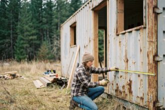 Femme mesurant un conteneur maritime en cours de transformation en tiny house sur un terrain rural