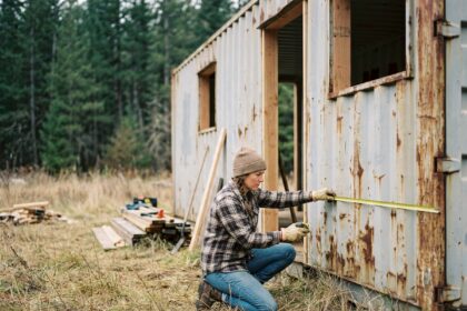 Femme mesurant un conteneur maritime en cours de transformation en tiny house sur un terrain rural